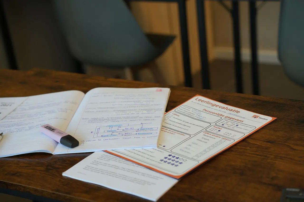 Tafel met werkbladen, schriften en een pen, zonder personen in beeld.